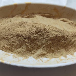 May include: A white ceramic bowl filled with a large amount of light brown powder.