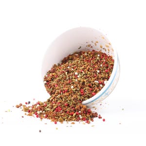 May include: A white bowl filled with a mixture of brown, green, red, and white spices. The bowl is tipped over, spilling the spices onto a white surface.