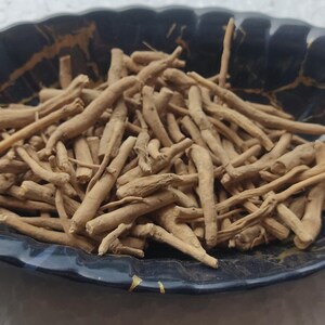 K&ouml;nnte beinhalten: Nahaufnahme einer Schale gef&uuml;llt mit getrockneten braunen Wurzeln. Die Schale ist schwarz mit goldenen Flecken und hat eine blattartige Form.