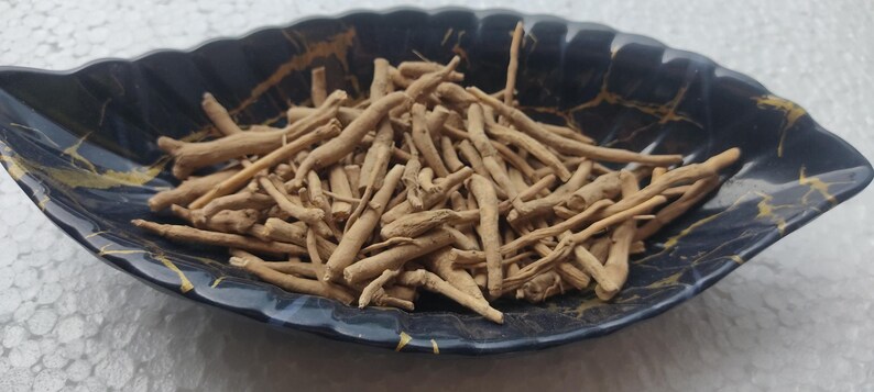 K&ouml;nnte beinhalten: Nahaufnahme einer Schale gef&uuml;llt mit getrockneten braunen Wurzeln. Die Schale ist schwarz mit goldenen Flecken und hat eine blattartige Form.