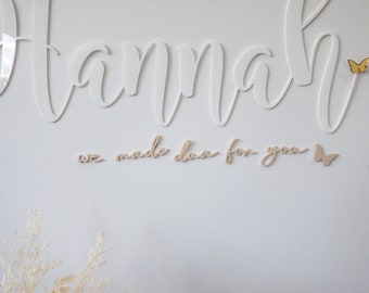 Może przedstawiać: Na białej ścianie białe, pisane kursywą imię "Hannah", ozdobione złotymi i jasnoróżowymi motylami. Pod imieniem napis "we made dua for you". Bukiet suszonych kwiatów w kolorze różowym i kremowym znajduje się w lewym dolnym rogu.