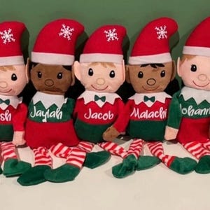 May include: Seven plush elf dolls with red hats, green and red outfits, and striped legs. Each doll has a different name embroidered on its chest: Asherah, Josh, Jaylah, Jacob, Malachi, Johann, and Aria. The hats have a white snowflake.