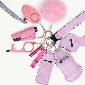 Può includere: Un portachiavi rosa con una varietà di articoli per la sicurezza e l'igiene, tra cui un allarme personale, un porta-sanitizer per le mani, un fischietto, un apribottiglie, uno strumento touch e un portachiavi con un pompon rosa soffice.