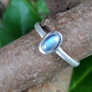 Op de afbeelding: Een zilveren ring met een blauwe ovale edelsteen. De ring ligt op een houten oppervlak.