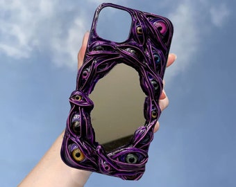 May include: Purple phone case with a mirror and multiple eyes. The case is made of a textured material and has a 3D effect.