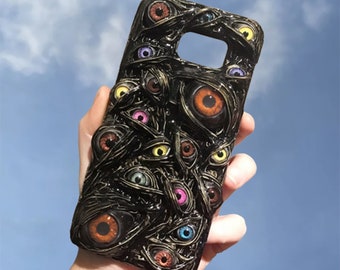 May include: A black phone case with a design of many colorful eyes on a black background. The eyes are 3D and appear to be bulging out of the case.