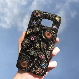May include: A black phone case with a design of many colorful eyes on a black background. The eyes are 3D and appear to be bulging out of the case.