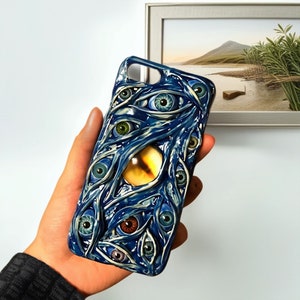 May include: A blue phone case with a design of multiple eyes, including a large yellow eye in the center.