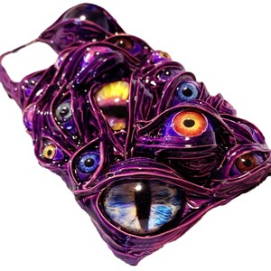 May include: A purple phone case with a design of many colorful eyes. The eyes are various shapes and sizes and are set against a dark purple background.