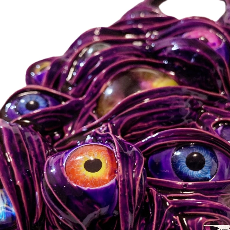 May include: A close-up of a purple, textured, 3D sculpture with multiple eyes. The eyes are painted in various colors, including blue, orange, and yellow.