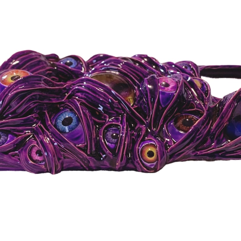 May include: A purple, textured, abstract sculpture with multiple eyes of different colors, including blue, orange, and brown.