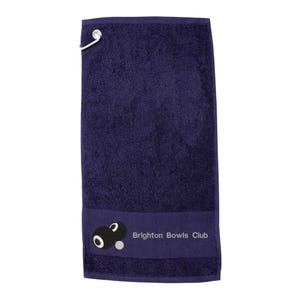 May include: A navy blue towel with a silver hanging loop. The bottom of the towel has a dark blue band with a graphic of two black bowling balls and the text "Brighton Bowls Club".
