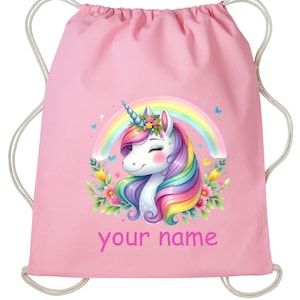 May include: Pink drawstring bag featuring a white unicorn with a rainbow mane and horn, surrounded by flowers and a rainbow. The bag has the text "your name" printed on it.