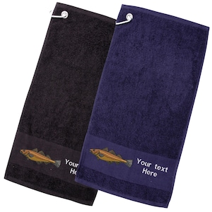 May include: Two golf towels, one black and one navy blue, with a fish embroidery. Each towel has a metal hook and a band at the bottom with the text "Your text Here". The fish is embroidered in shades of gold and brown.