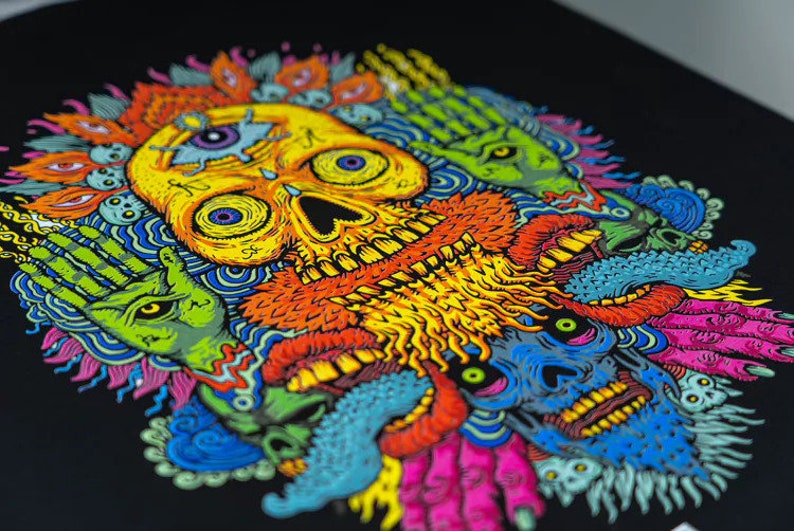 May include: A colorful skull with a third eye and a beard surrounded by other colorful creatures with eyes and teeth. The background is black.
