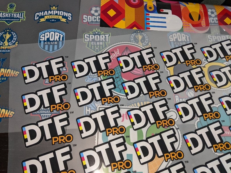 May include: Close-up of multiple white stickers with the text "DTF PRO" in black letters. The stickers feature a small yellow, blue, and red flag design.