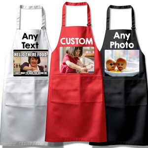 Puede incluir: Tres delantales blancos, rojos y negros con bolsillos. El delantal blanco tiene el texto "Any Text" y una imagen de meme de una mujer que dice "Hello there food, I can't wait to have you inside me". El delantal rojo tiene el texto "CUSTOM" y una foto de una niña con un vestido rosa. El delantal negro tiene el texto "Any Photo" y una foto de dos huevos con caras dibujadas.