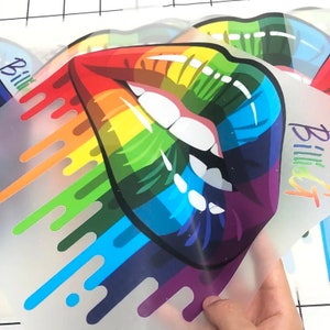 May include: A rainbow-colored graphic of a pair of lips with dripping paint. The lips are outlined in black and have a white interior. The dripping paint is in the colors of the rainbow, with red, orange, yellow, green, blue, indigo, and violet.