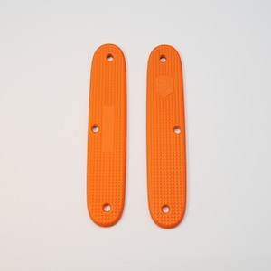 Könnte beinhalten: Zwei orangefarbene Kunststoffschalen für ein Taschenmesser. Die Schalen haben eine strukturierte Oberfläche und sind für ein Standard-Taschenmesser ausgelegt.