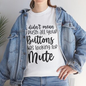 Peut inclure: T-shirt blanc avec l'inscription noire "I didn't mean to push all your Buttons was looking for Mute". Porté avec une veste et un jean en jean bleu.