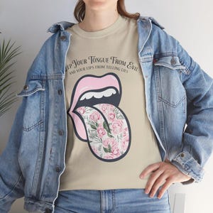 Może przedstawiać: Beżowa koszulka z grafiką różowego języka z kwiatowym wzorem i napisem "KEEP YOUR TONGUE FROM EVIL AND YOUR LIPS FROM TELLING LIES". Projekt jest wyśrodkowany na koszulce.