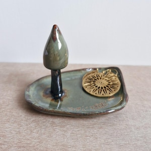 May include: A ceramic ring holder shaped like a tree with a green glaze and a black base. The holder is on a matching green glazed ceramic dish with a gold-toned earring in the shape of a star.