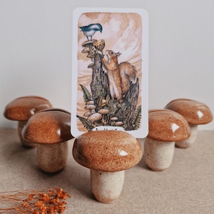 May include: Six ceramic mushroom-shaped card holders in brown and white with a card featuring a watercolour illustration of a squirrel and a bluebird perched on a mushroom.