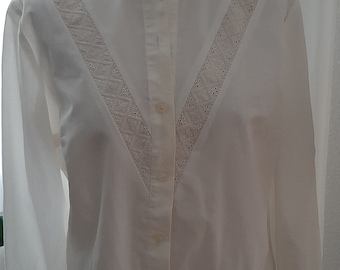 May include: A white long-sleeved blouse with a ruffled collar and a V-shaped lace design on the front.