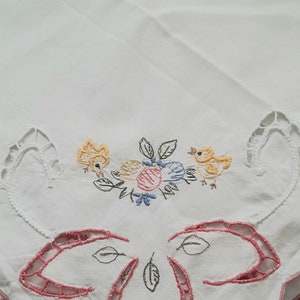 Könnte beinhalten: Weiße Tischdecke mit rosa und blauen gestickten Blumen und Vögeln. Die Tischdecke hat einen gewellten Rand mit einem rosa Saum.