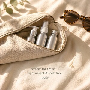 May include: A beige travel pouch with a gold zipper holds three silver bottles: a pump bottle, a spray bottle, and a small bottle with a screw-on cap. Tortoiseshell sunglasses rest nearby. The text reads: "Perfect for travel - lightweight & leak-free."