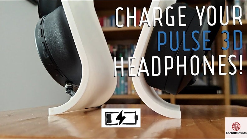 Op de afbeelding: Een witte 3D-geprinte standaard voor het opladen van Sony Pulse 3D draadloze hoofdtelefoons. De standaard is gebogen met een kleine uitsparing aan de onderkant voor de oplaadkabel. De hoofdtelefoon rust op de standaard met de oplaadpoort naar beneden gericht. De tekst "CHARGE YOUR PULSE 3D HEADPHONES!" staat in witte letters op een zwarte achtergrond boven de standaard. Een batterijpictogram met een bliksem is onder de standaard.