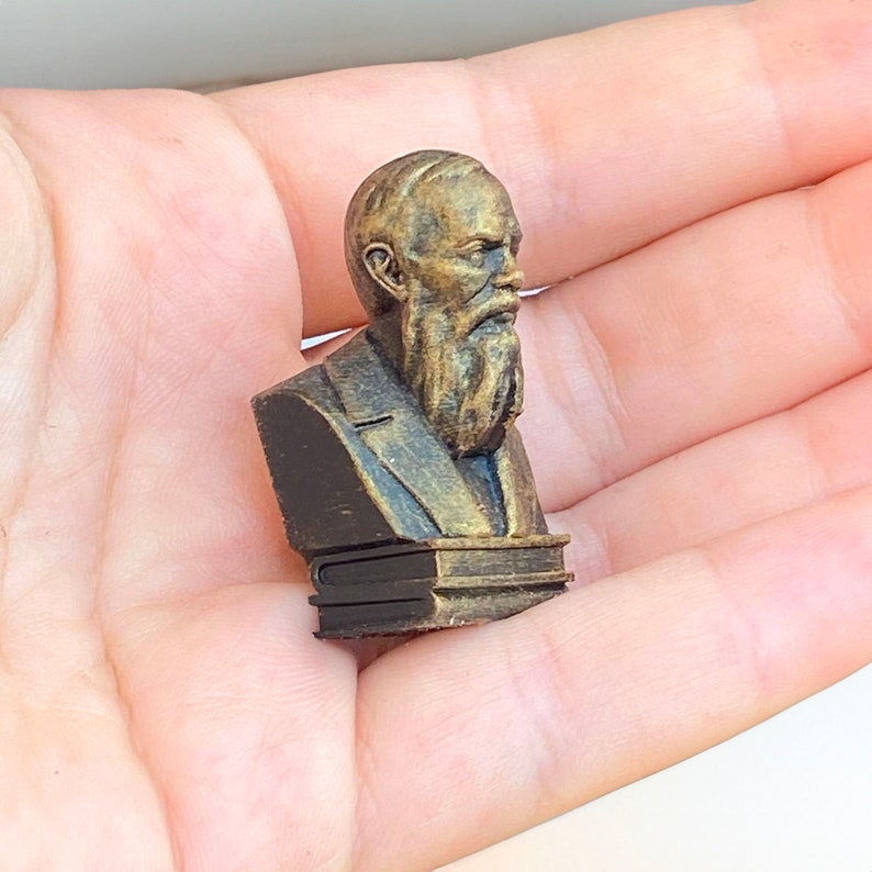 May include: A wooden bust of a man with a beard and mustache, wearing a suit and tie. The bust is painted in a bronze color and is mounted on a wooden base.