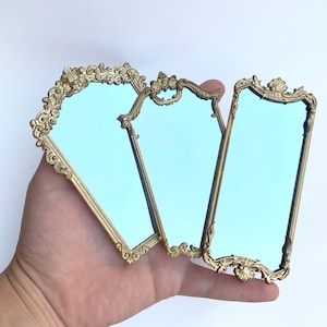 May include: Three ornate gold-colored framed mirrors with blue glass. The mirrors are arranged in a fan shape.