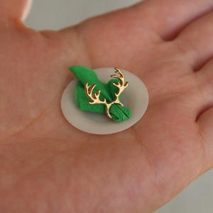 Puede incluir: Un anillo de servilleta de reno dorado que sostiene una servilleta verde en un plato blanco.