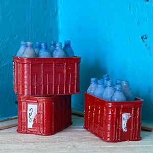 May include: Two red crates stacked on top of each other, filled with blue glass bottles. The top crate has the number "523" written on the side.