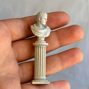 May include: A white plaster bust of a man with short hair on a white pedestal with fluted columns.