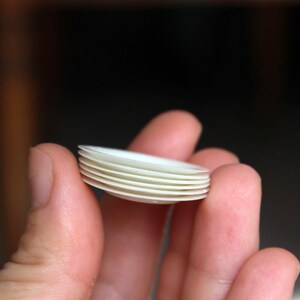 Puede incluir: Una pila de platos peque&ntilde;os de cer&aacute;mica blanca, probablemente para una casa de mu&ntilde;ecas o uso en miniatura.