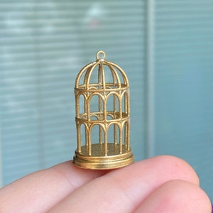 May include: A gold-colored metal birdcage with a decorative design. The cage is small and has a round base.
