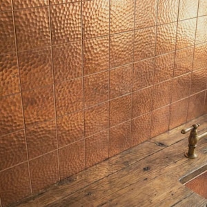 May include: A copper kitchen backsplash with a hammered texture, installed in a grid pattern. The copper sink and faucet have a vintage design. The countertop is made of reclaimed wood.