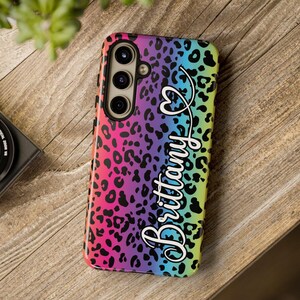 May include: A phone case with a rainbow leopard print design. The case features the name "Brittany" in a cursive font with a heart-shaped stethoscope graphic. The case has a black border and a camera cutout.