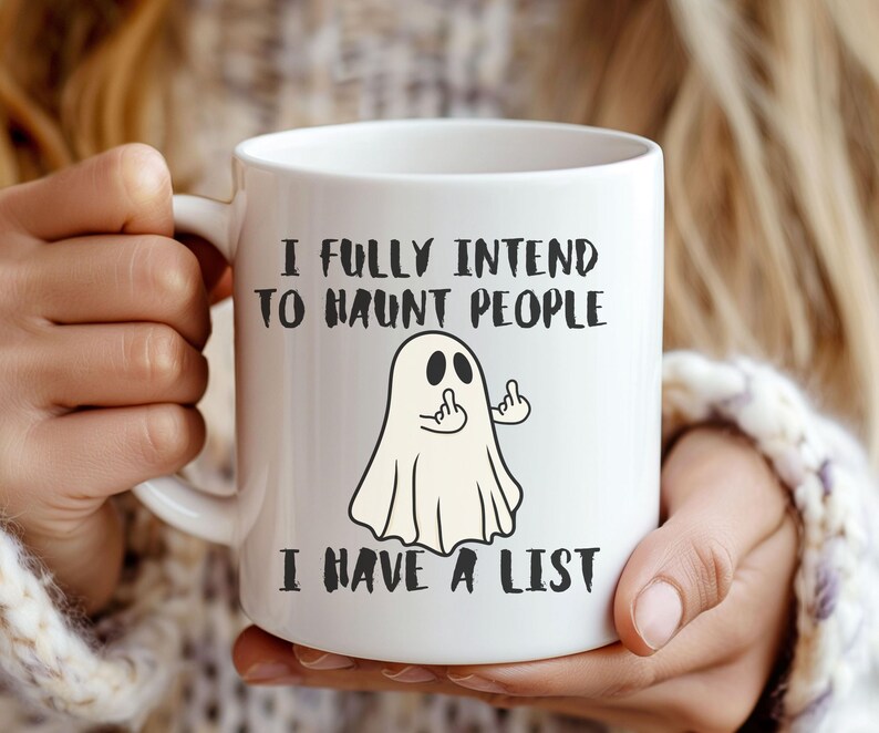 Puede incluir: Taza de cer&aacute;mica blanca con el texto "I FULLY INTEND TO HAUNT PEOPLE I HAVE A LIST" y un fantasma de dibujos animados haciendo un gesto grosero. La taza tiene un asa blanca y la sostiene una persona.