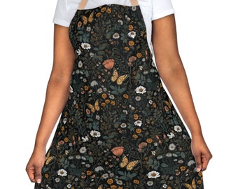 May include: Black apron with a floral and butterfly pattern. The apron features a dark background with a repeating design of white daisies, orange poppies, and yellow butterflies. The apron has a tan neck strap.