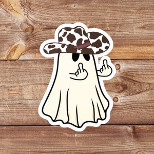 May include: A sticker featuring a cartoon ghost wearing a brown and white cow print cowboy hat. The ghost is giving the middle finger with both hands. The ghost is white with black eyes and a black outline.
