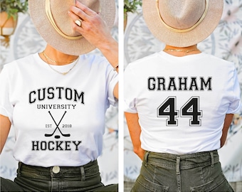 May include: White t-shirt with black text and hockey stick graphic on the front. The back of the shirt has black text "GRAHAM" and the number "44" in a varsity style font.