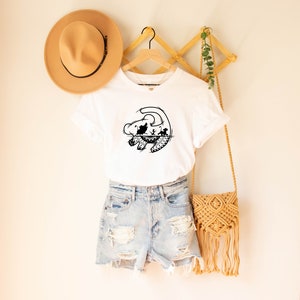 May include: White t-shirt with a black silhouette of Simba from The Lion King. The silhouette shows Simba as a cub with his parents Mufasa and Sarabi.