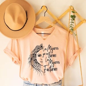 May include: A peach-colored t-shirt with a black and white illustration of a woman's face and the text "Las Mujeres ya no Lloran Las Mujeres Facturan".