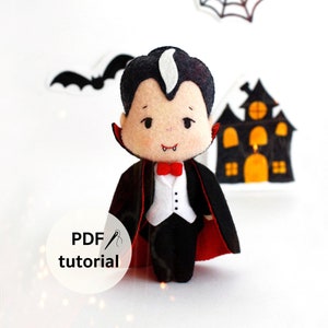 May include: A felt vampire doll wearing a black suit with a red cape and a white shirt. The doll has a white face with black eyes and a red mouth. The doll is standing on a white surface with a black bat and a spiderweb in the background. The text "PDF tutorial" is on a white circle with a needle and thread.