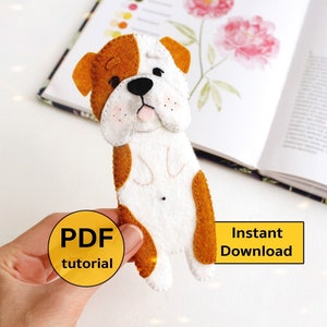 Puede incluir: Un marcapáginas de fieltro con forma de bulldog de color marrón y blanco. El marcapáginas está sobre un libro con una ilustración floral. El texto "PDF tutorial" y "Instant Download" está en la imagen.