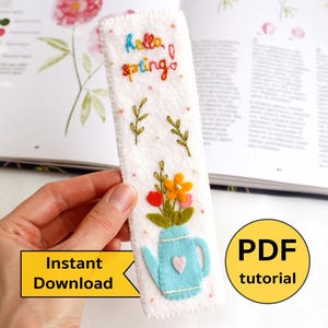 Puede incluir: Marcapáginas de fieltro blanco con bordado de colores de flores en una tetera azul. El marcapáginas dice "hello spring" en bordado de colores. Tutorial PDF incluido.