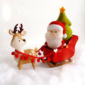 Felt Christmas toys - Santa Claus standing near the sleigh, reindeer Rudolph and Christmas tree on the snow